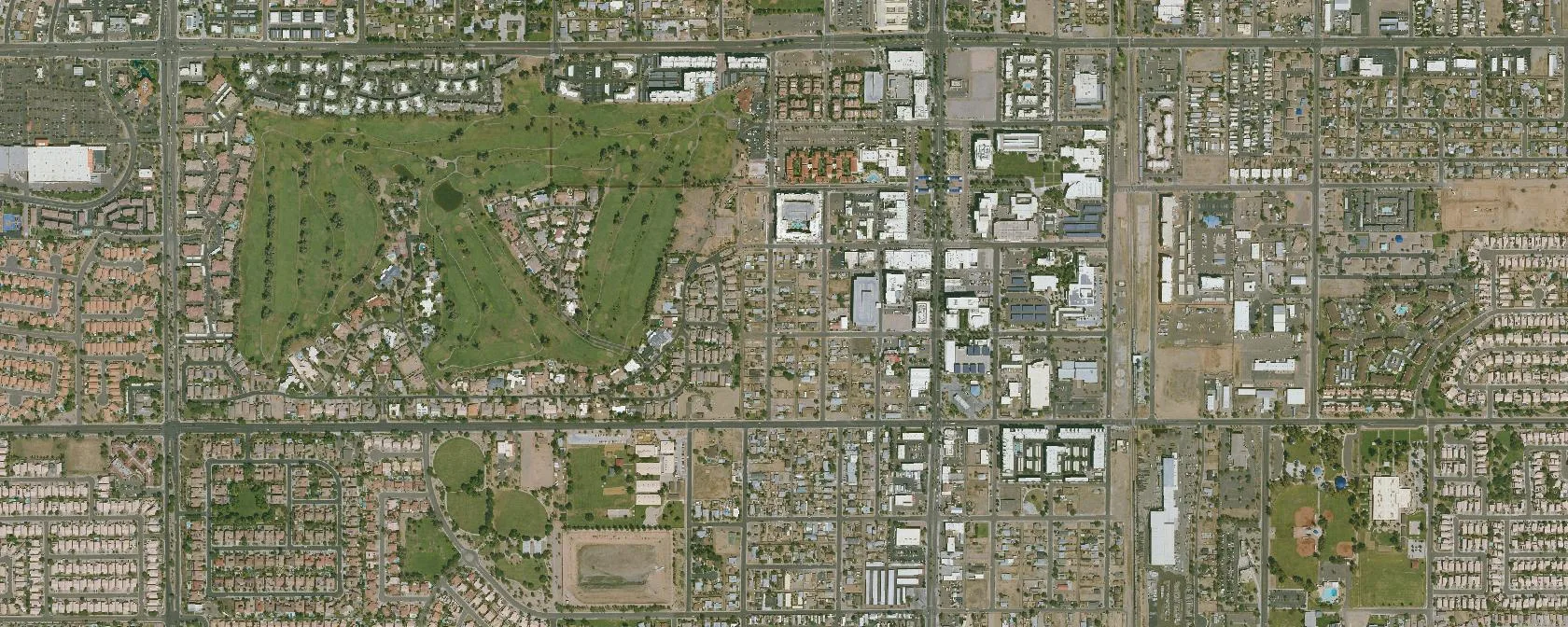 Aerial of Chandler, AZ: planned suburban grid streets, mixed residential and commercial blocks, golf course, the actual operating territory of Waymo's autonomous robotaxi fleet. A single block is outlined teal, the kind of pickup verdict an autonomous agent acts on at decision time.